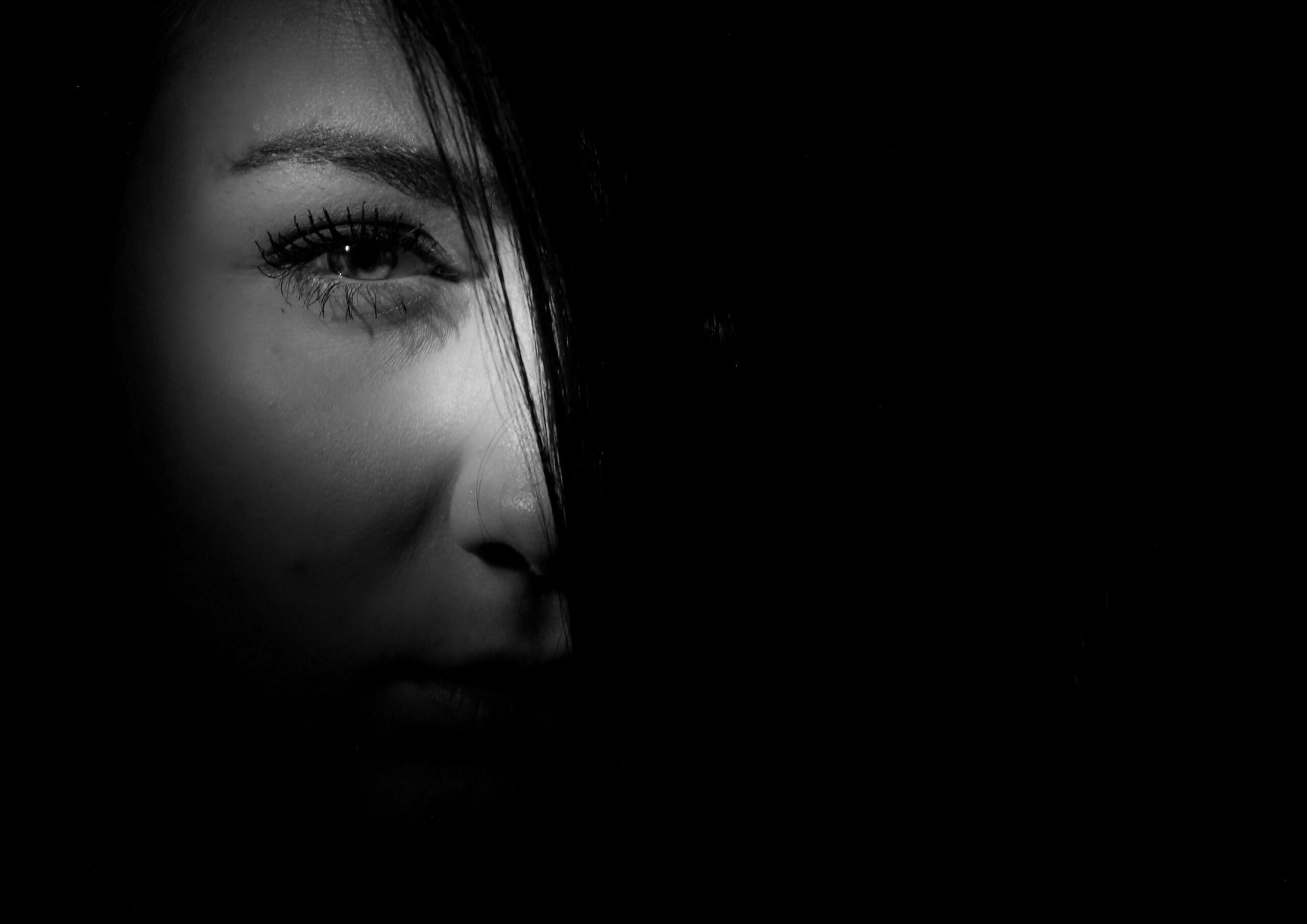 Mysterious black and white portrait of a woman's face in dramatic lighting.