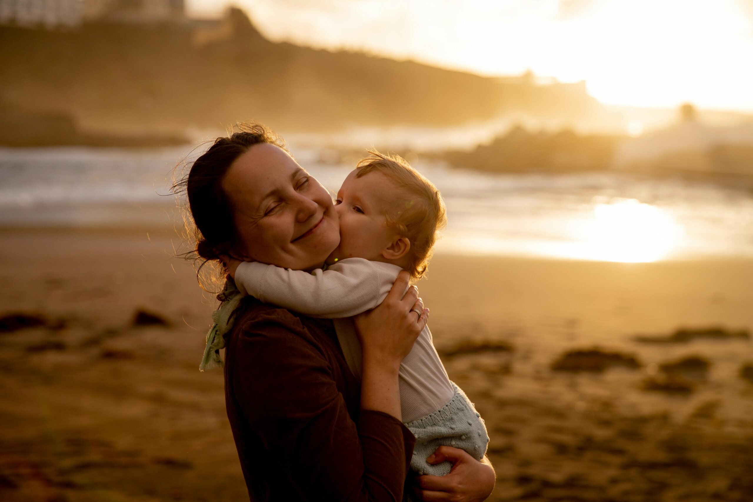 A joyful mother and child bonding moment captured on a beach at sunset.